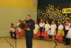 Marszałek Leszek Zegzda stoi przed mikrofonem z bukietem czerwonych róż w ręku. W tle grupa dzieci.