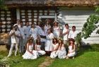 Grupa chłopców i dziewcząt ubranych na biało i z wiankami na tle drewnianej chaty