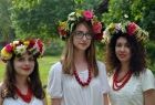 Trzy młode dziewczyny w białych bluzkach i czerwonych koralach z wiankami ze świeżych kwiatów na głowie