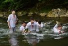 Grupa chłopców w mokrych ubraniach łowi wianki w rzece